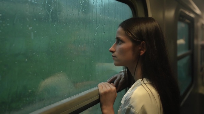 火车窗外下着大雨。女人或女孩站在窗边，看着雨滴顺着玻璃流下来。在雨中乘火车去山里旅行的梦幻气氛。