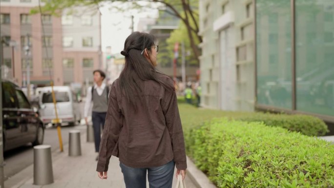 日本东京，亚洲女游客走在城市街道上，环视城市景观。