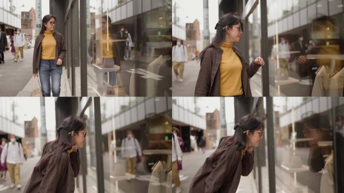 年轻的亚洲女游客走在街上，看着商店橱窗里的衣服。