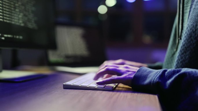 女黑客在黑暗的办公室里使用台式电脑的特写镜头