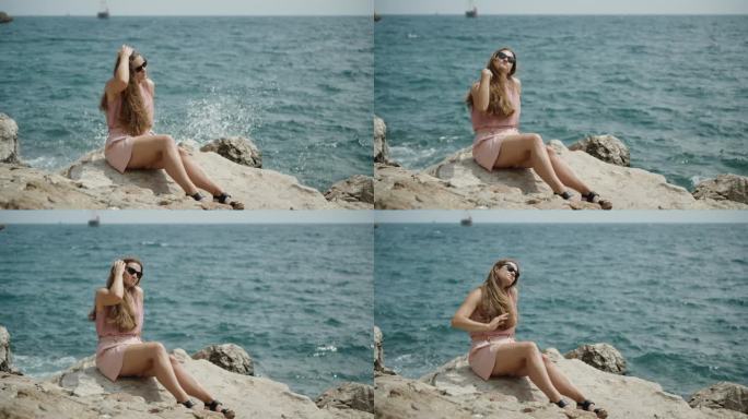 一个穿着粉色短裤的年轻女子坐在岩石上，背景是海浪和水花。她整理了一下头发