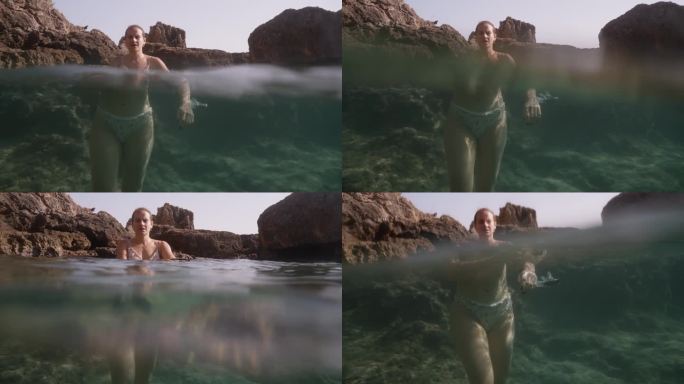 一名年轻女子站在岩石上透明的海水中，相机放置在水边，捕捉水面上和水下的画面，放大了水下场景。