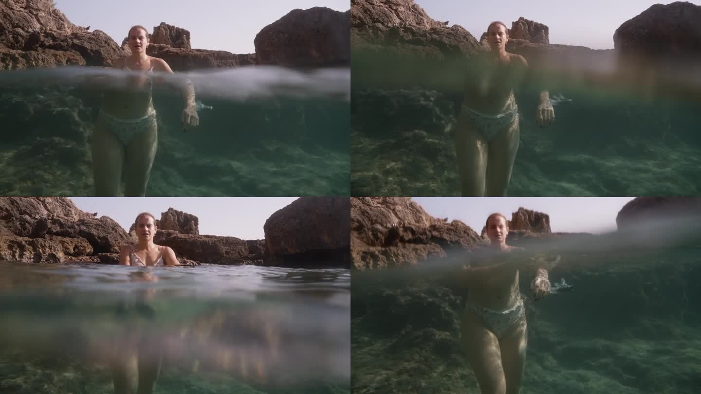 一名年轻女子站在岩石上透明的海水中，相机放置在水边，捕捉水面上和水下的画面，放大了水下场景。