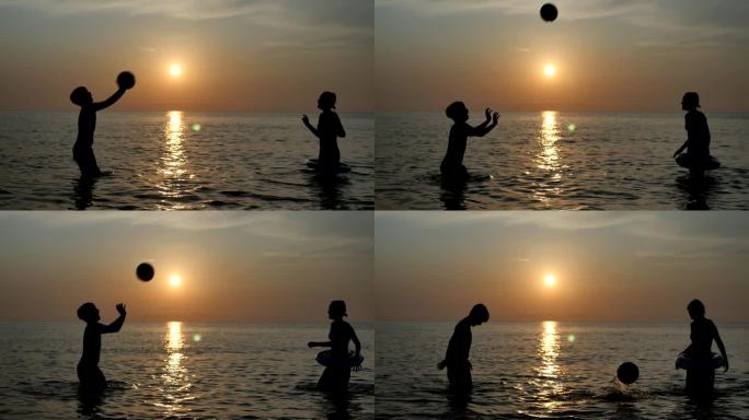 日落时分，一男一女两个少年站在海边打排球的剪影。快乐的弟弟和妹妹用手掌把球推向对方。水排球