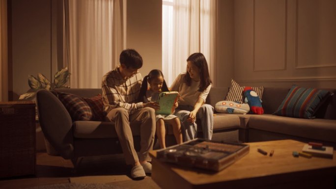 一家三口在客厅使用科技的广角镜头:韩国父母和他们的小女儿一起在数码平板电脑上玩游戏，笑着玩