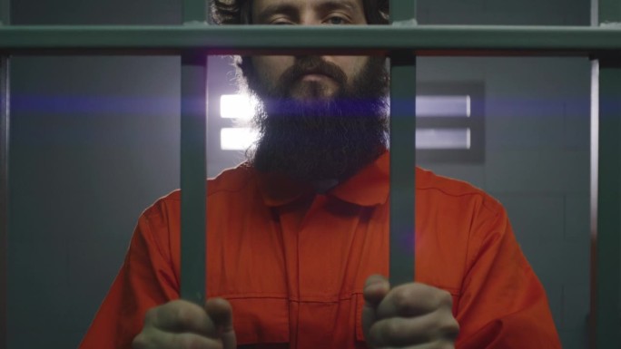 身穿橙色制服、戴着手铐的男性罪犯站在牢房里