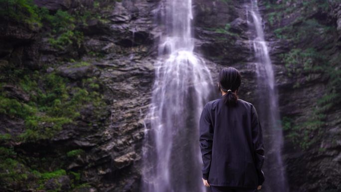 女性游客背影面向山水感受亲近自然山峰瀑布