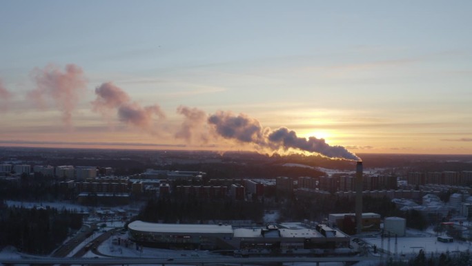 无人机拍摄的区域供暖设施冒烟的画面，背景是冬季日落时下雪的住宅背景。
