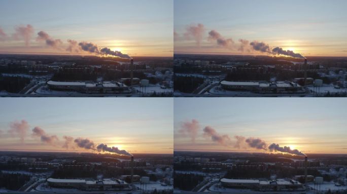 无人机拍摄的区域供暖设施冒烟的画面，背景是冬季日落时下雪的住宅背景。