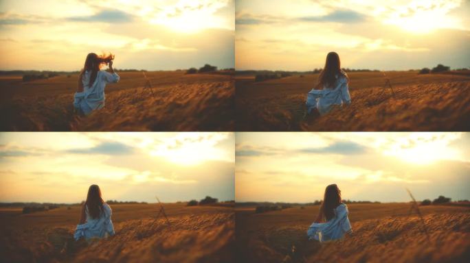 美丽的女人在橙色的天空下走在小麦丛中