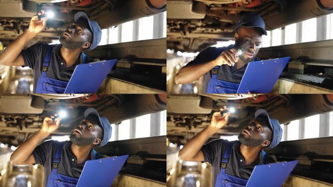 非洲男机械师拿着手电筒和检查坑里的检查清单检查火车的底盘