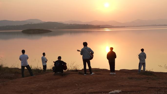 夕阳下水边弹吉他的青年