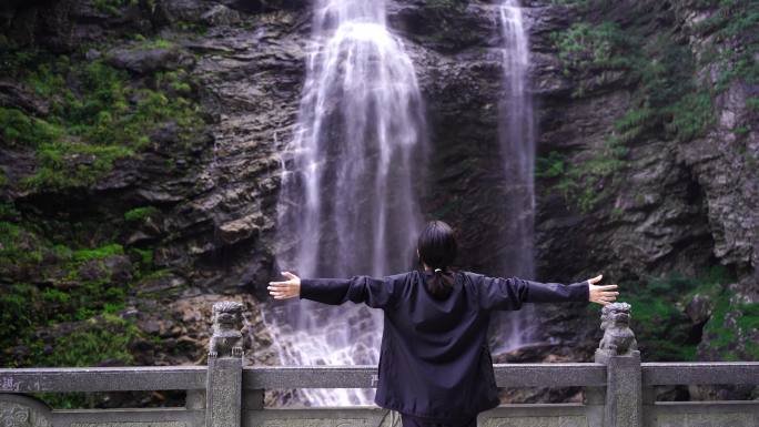 女性游客背影面向山水感受亲近自然山峰瀑布