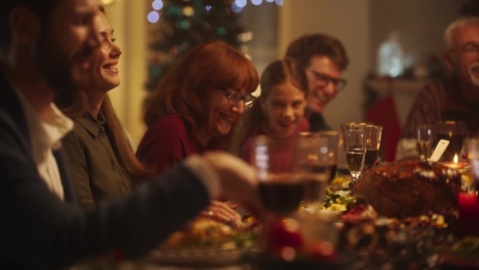 亲密的家庭晚餐设置与一群不同的亲戚庆祝圣诞节，在装饰客厅的大桌子上一起用餐。亲人谈笑风生，享受美食