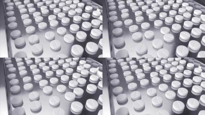 在现代制药厂，白色药丸在传送带上移动。片剂和胶囊制造工艺。药品生产线特写镜头。批量生产概念。循环