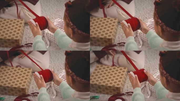 小女孩帮妈妈用红丝带包圣诞礼物