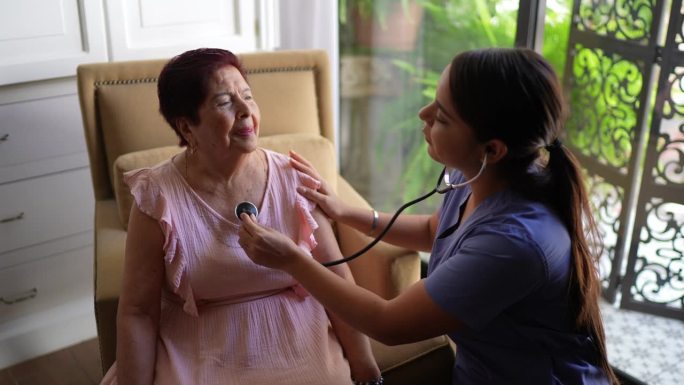 护理员在养老院倾听一位老年妇女的心跳