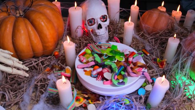 节日背景，骷髅手与彩色糖果和糖果旋转盘周围的蜡烛