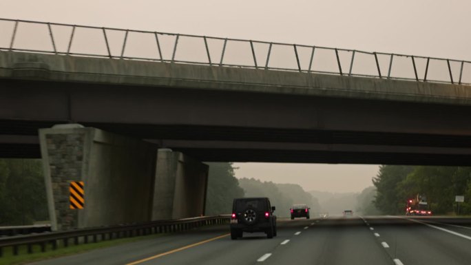 在桥下行驶:汽车在通往马里兰州的烟雾弥漫的道路上，从人行道下面经过。驾驶板摄影机运动