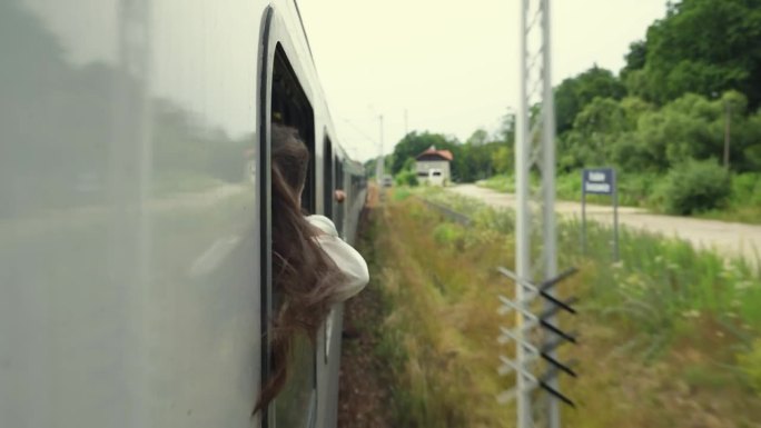 在行驶中的火车上，年轻的女人或女孩把手和头伸出窗外，微笑着。喜欢坐火车旅行，夏天去山里旅行。