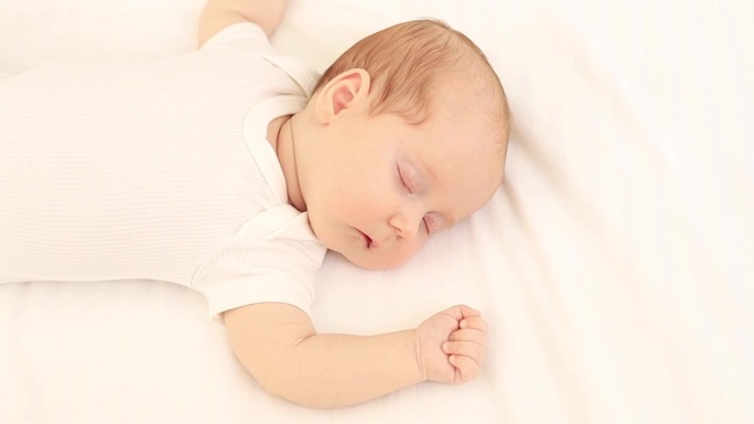 一个刚出生的婴儿穿着白色的紧身衣睡在家里的棉床上，特写肖像，文字空间