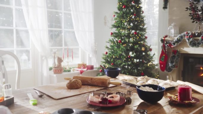 宁静的下雪的圣诞节早晨:在一个装饰着圣诞树、壁炉和礼物的现代房子的角落里，一张桌子上放着烘焙原料和器