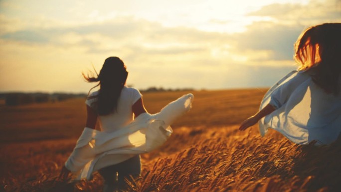 夕阳下，年轻女子和朋友在金黄色的麦田里奔跑