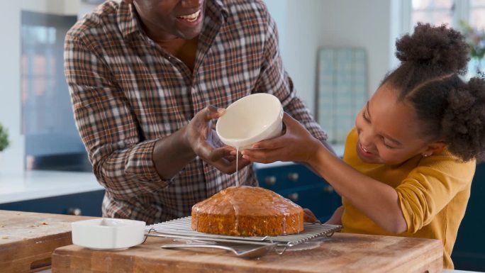 父亲和女儿在厨房用糖霜装饰蛋糕的家庭照片