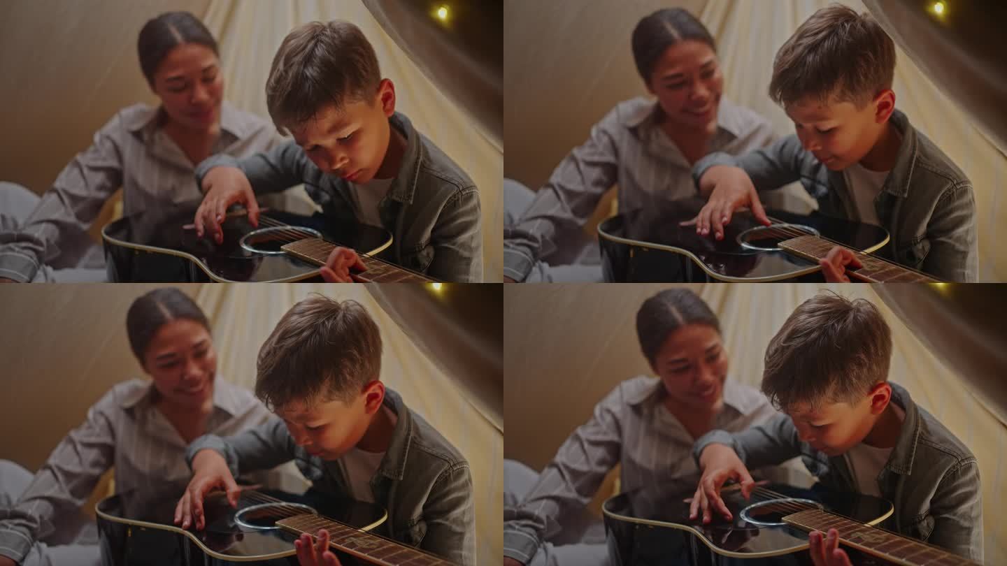 可爱的小男孩给他的妈妈弹吉他，一起坐在游戏帐篷里睡觉