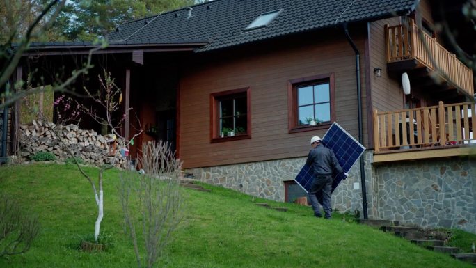 一名工人正在搬运太阳能板，以便在房屋上安装太阳能模块系统。