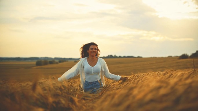 微笑的女人在小麦农场跑步，享受日落