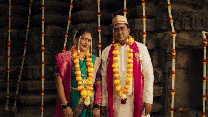 幸福的印度夫妇看着相机，在他们的传统婚礼上拍照。新娘和新郎穿着漂亮的彩色衣服庆祝他们的爱情和结合的真
