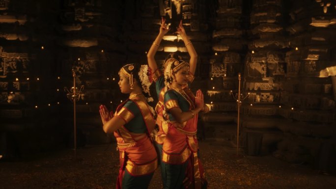 三位富有表现力的年轻印度舞者在古庙内表演民间舞蹈的慢动作肖像。穿着传统服装的妇女穿着五颜六色的纱丽跳