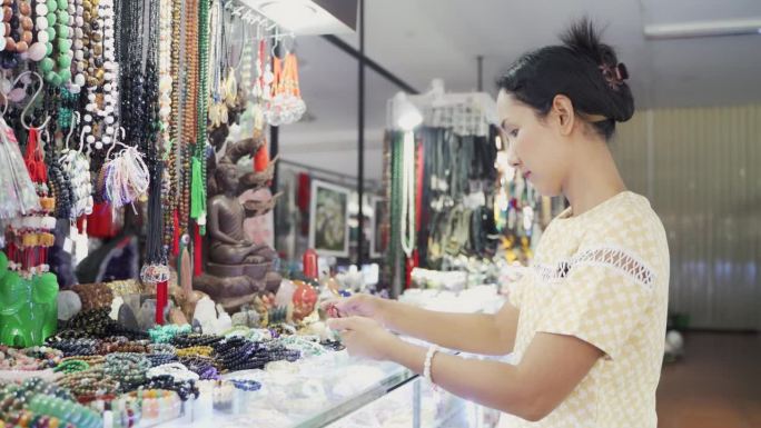 亚洲妇女在饰品店选购手工制作的手链或手镯。