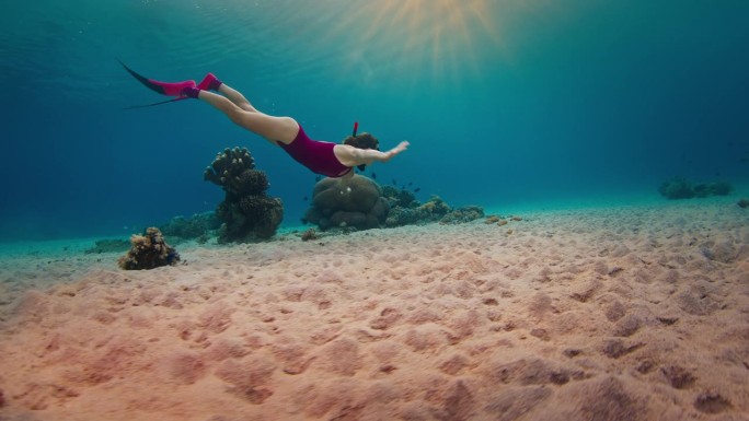 一名身穿粉色潜水服的女子在日落时分在印度尼西亚的热带海洋中滑翔，享受水下游泳的乐趣