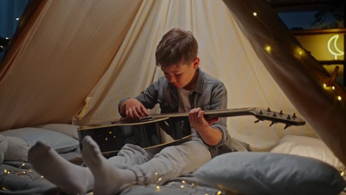 可爱的小男孩在帐篷里弹吉他，睡觉前在地板上玩露营