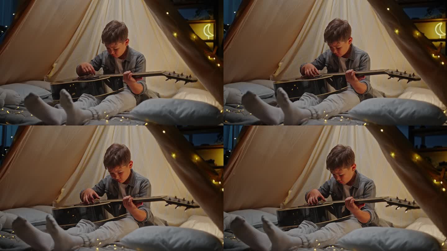 可爱的小男孩在帐篷里弹吉他，睡觉前在地板上玩露营