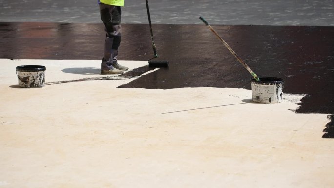建筑工人用滚筒刷在混凝土表面涂煤焦油或沥青材料