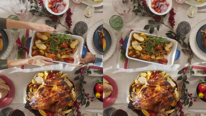 竖屏:装饰高雅的圣诞宴会桌，烤火鸡，蔬菜，烤土豆，甜点。从上往下看，人们把盘子放在家里的餐桌上