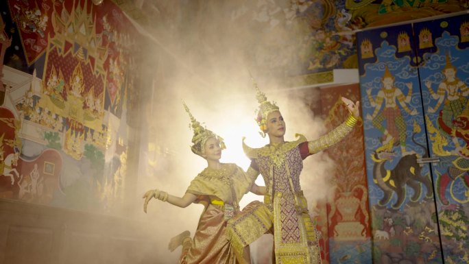 美丽的亚洲女子穿着泰国传统服装，站在公共场所墙上的泰国画前与男子一起跳舞。