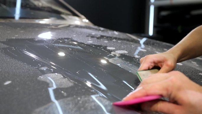 一位女士和一位男士用塑料刮刀在新车上涂保护膜。