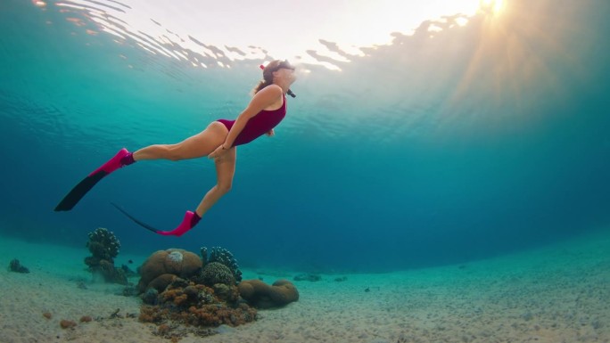 一名身穿粉色潜水服的女子在日落时分在印度尼西亚的热带海洋中滑翔，享受水下游泳的乐趣