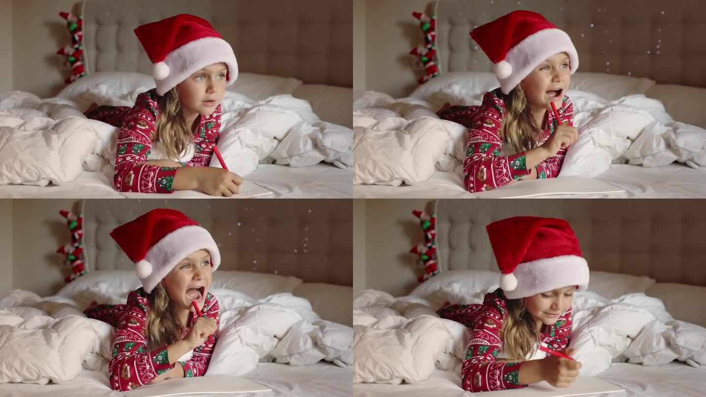 圣诞快乐，新年快乐。快乐的小女孩躺在床上装饰着家里的红帽子、绒球睡衣做想着给圣诞老人的信。孩子在给圣