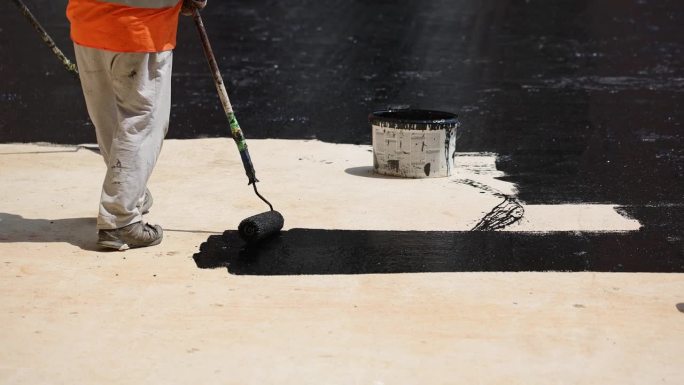 建筑工人，用滚筒刷在混凝土表面涂煤焦油或沥青材料