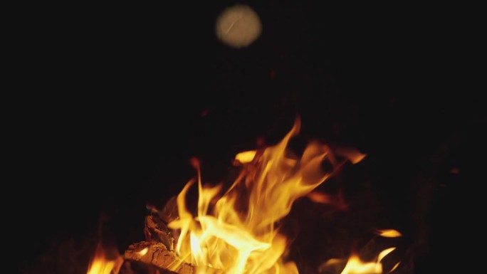 慢镜头，微距，DOF:在一片漆黑中，橙色的营火闪烁着明亮的火花。橘黄色的火焰吞没了营火中的煤炭，火花