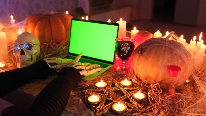 从侧面看，瘦骨嶙峋的双手在笔记本电脑键盘上戏剧性地打字，绿屏是万圣节的庆祝属性之一
