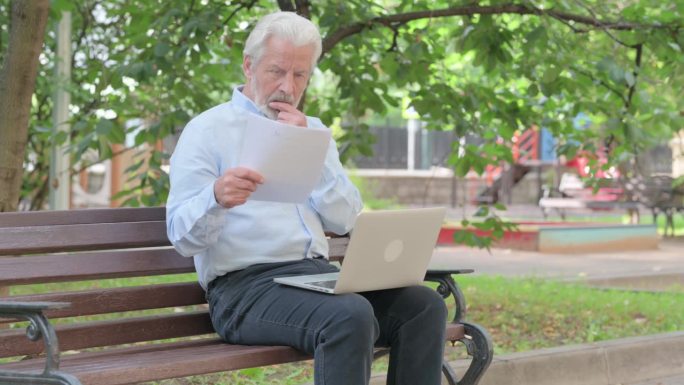 老年老人在户外阅读合同和使用笔记本电脑时心情烦乱