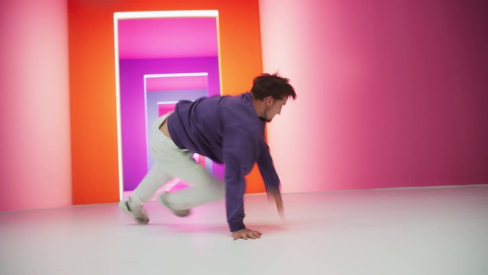 年轻和运动的B-Boy霹雳舞打破节奏在一个彩色抽象霓虹灯工作室。精力充沛的时尚男子练习自由式编舞为即