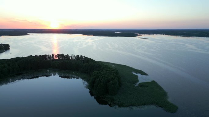 日落时分，无人机在平静湖面环绕的小半岛上空盘旋