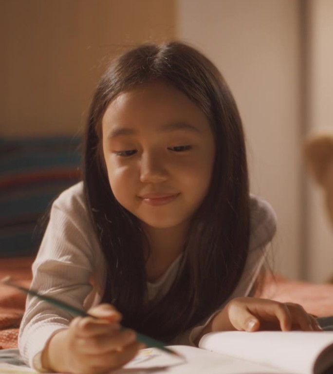 垂直屏幕:可爱的韩国小女孩躺在床上，用钢笔和铅笔在笔记本上画画。快乐和创造性的女孩子在家里在她的房间